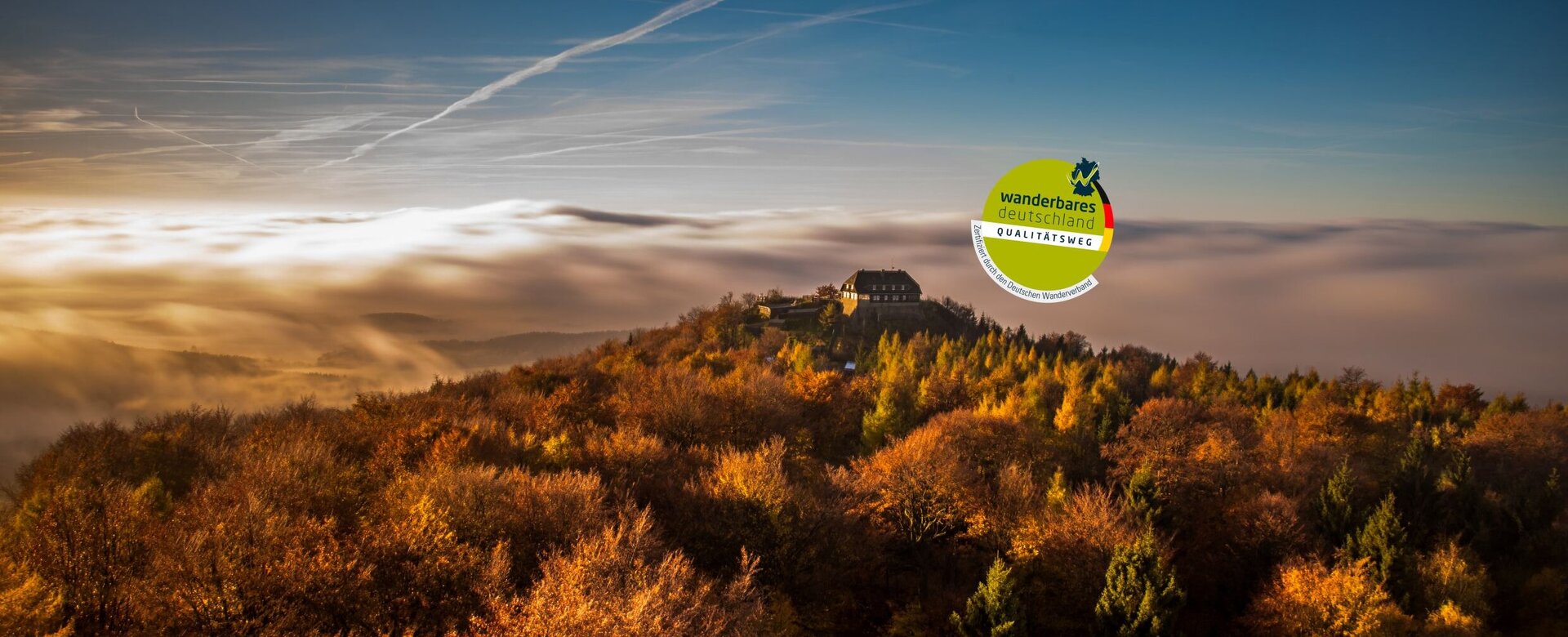 Berggipfel mit Gebäude, dahinter Wolken 